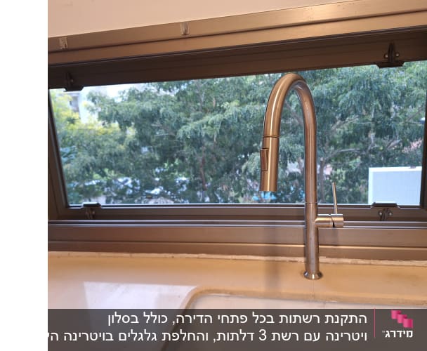 ברז נירוסטה ליד חלון אלומיניום עם נוף עצים
